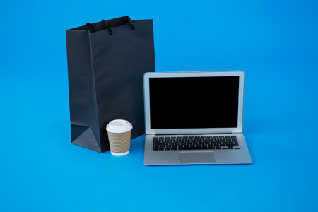 Shopping bag and disposable coffee cup with laptop against blue backgroundの写真素材