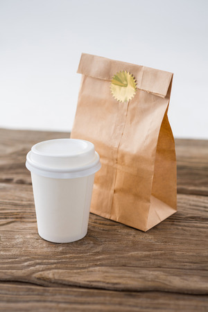 Disposable coffee cup and parcel bag on wooden tableの写真素材