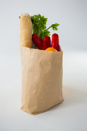 Fruits and vegetables in brown grocery bag against white backgroundの写真素材