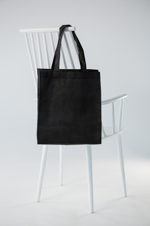 Black bag hanging on a white chair against white backgroundの写真素材