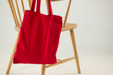 Red bag hanging on a wooden chair against white backgroundの写真素材