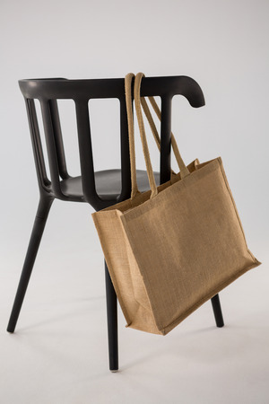 Jute bag hanging on a black chair against white backgroundの写真素材