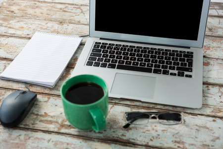 Laptop, mouse, spectacle and notepad with cup of coffee on wooden tableの写真素材