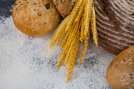Close-up of bread loaves with wheat and flour on black surface