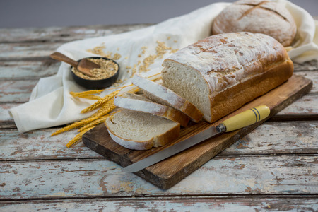 Bread loaf with knife, wheat grains and oats on wooden surface