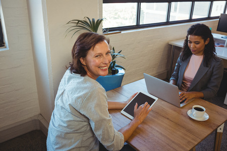 Business executives using laptop and digital tablet on table in officeの写真素材