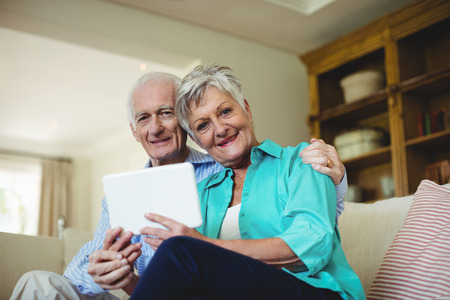 Portrait of senior couple using digital tablet in living room at homeの写真素材
