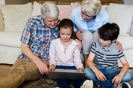 Grandchildren using laptop with their grandparents at home