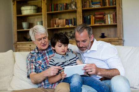 Boy using digital tablet with his father and grandfather in living room at home