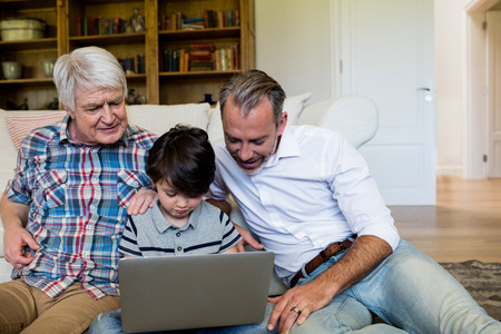 Boy using laptop with his father and grandfather in living room at homeの写真素材