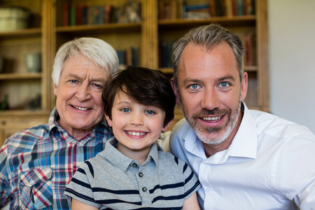 Portrait of smiling boy with his grandfather and father in living room at homeの写真素材