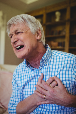 Senior man suffering from chest pain in living room at homeの写真素材