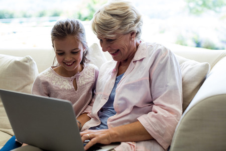 Granddaughter and grandmother using laptop in living room at homeの写真素材