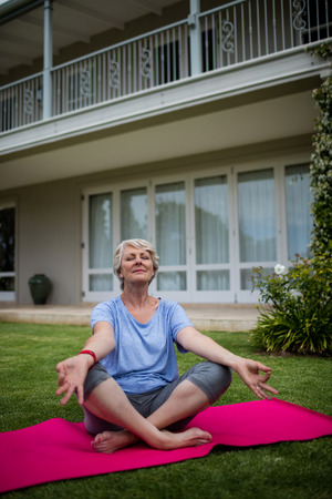 Senior woman practising yoga on exercise mat in lawnの写真素材