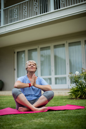 Senior woman practising yoga on exercise mat in lawnの写真素材