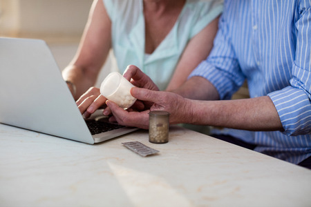 Mid section of senior couple checking medicine on laptop in kitchen at home