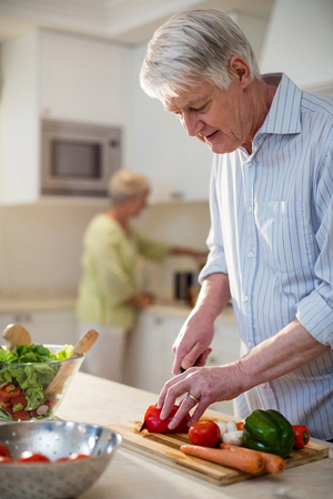 Senior man cutting vegetables for salad in kitchenの写真素材