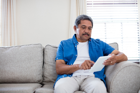 Senior man using digital tablet in living room at homeの写真素材