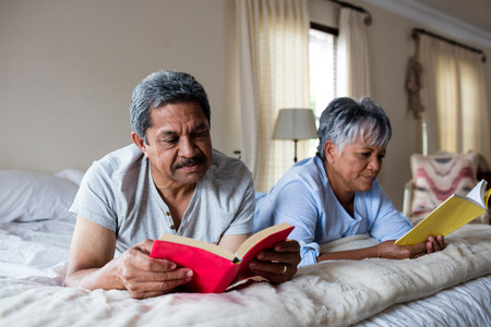 Senior couple reading books on bed at homeの写真素材