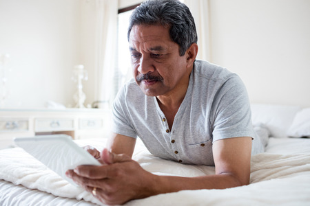 Senior man using digital tablet on bed at homeの写真素材