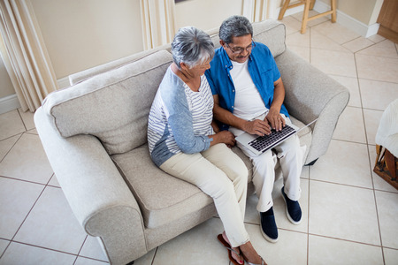 Senior couple using laptop in living room at homeの写真素材