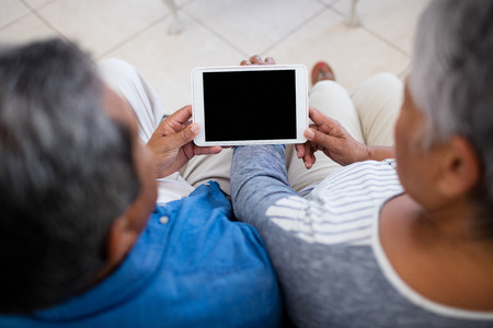 Senior couple using digital tablet while sitting in the living room at homeの写真素材