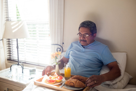 Senior man having breakfast on bed in bedroomの写真素材