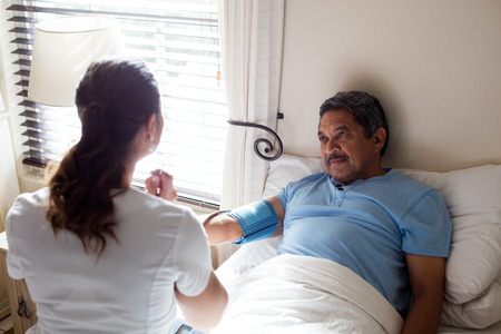 Doctor checking blood pressure of senior woman in bedroom at homeの写真素材