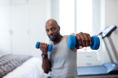 Man exercising with dumbbells in bedroom at homeの写真素材