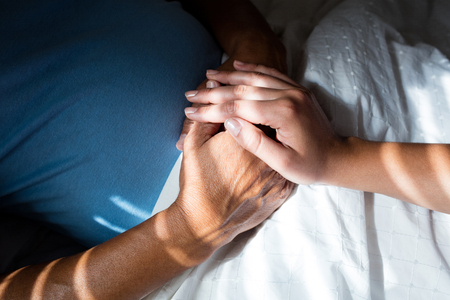 Close-up of doctors hand consoling senior patient in bedroom at homeの写真素材