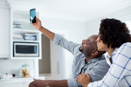 Happy couple taking selfie on mobile phone in living room at homeの写真素材