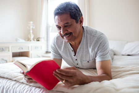 Smiling senior man reading a novel in living room at homeの写真素材