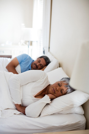 Senior couple sleeping together on bed in bedroom at homeの写真素材