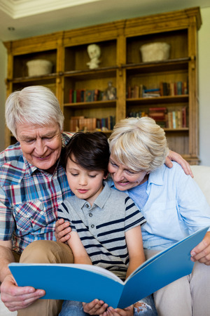 Grandparents and grandson looking at book in living room at homeの写真素材