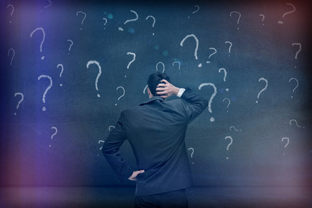 Rear view of a doubtful businessman looking at various question marks drawn on a grey wall 3dの写真素材