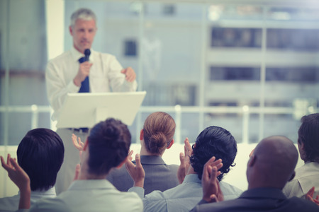 Business team applaud a mature businessman who is holding a microphone with focus on the business teamの写真素材