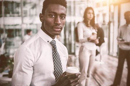 Portrait of businessman with colleagues holding disposable coffee cup in officeの写真素材