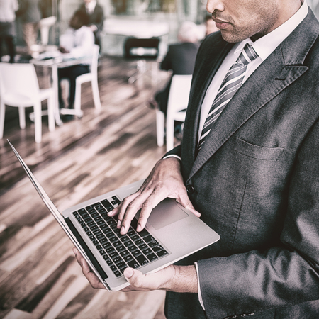 Focused businessman using laptop while standing in officeの写真素材