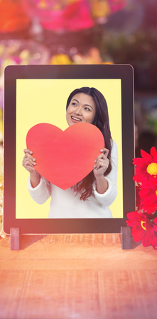 Smiling Asian woman holding paper heart against digital technology with flowersの写真素材
