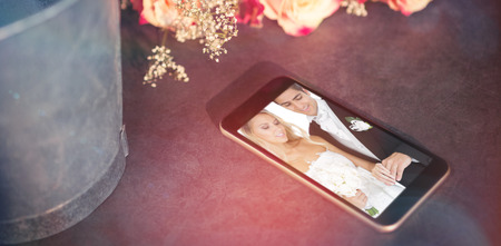 High angle view of mobile phone by flower against smiling young married couple wearing wedding ringsの写真素材