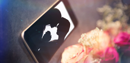 High angle view of smart phone white flower against silhouette of affectionate couple face to face holding handsの写真素材