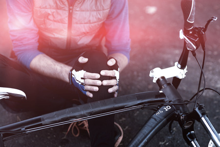 Midsection of male biker in pain holding his injured leg on countryside roadの写真素材