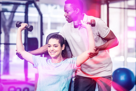 Athletic woman lifting weights helped by trainer at gymの写真素材