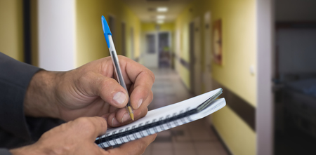 Close up of man writing in spiral book against vacant corridor