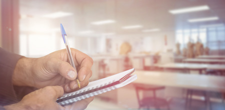 Close up of man writing in spiral book against empty class roomの写真素材