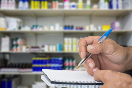 Close up of man writing in notepad against medicine in shopの写真素材