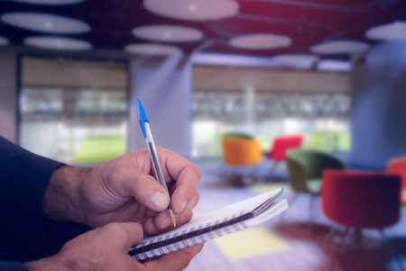 Close up of man writing in spiral book against collegeの写真素材