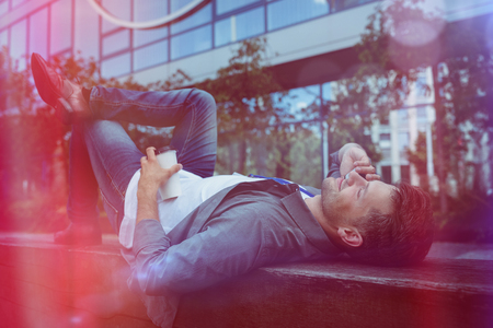Handsome business executive lying talking on mobile phone while lying on retaining wallの写真素材