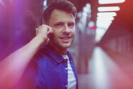 Portrait of handsome man speaking on mobile phone at railway platformの写真素材