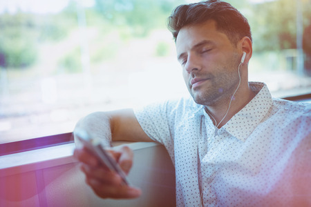 Handsome man with closed eyes listening music on mobile phone in train